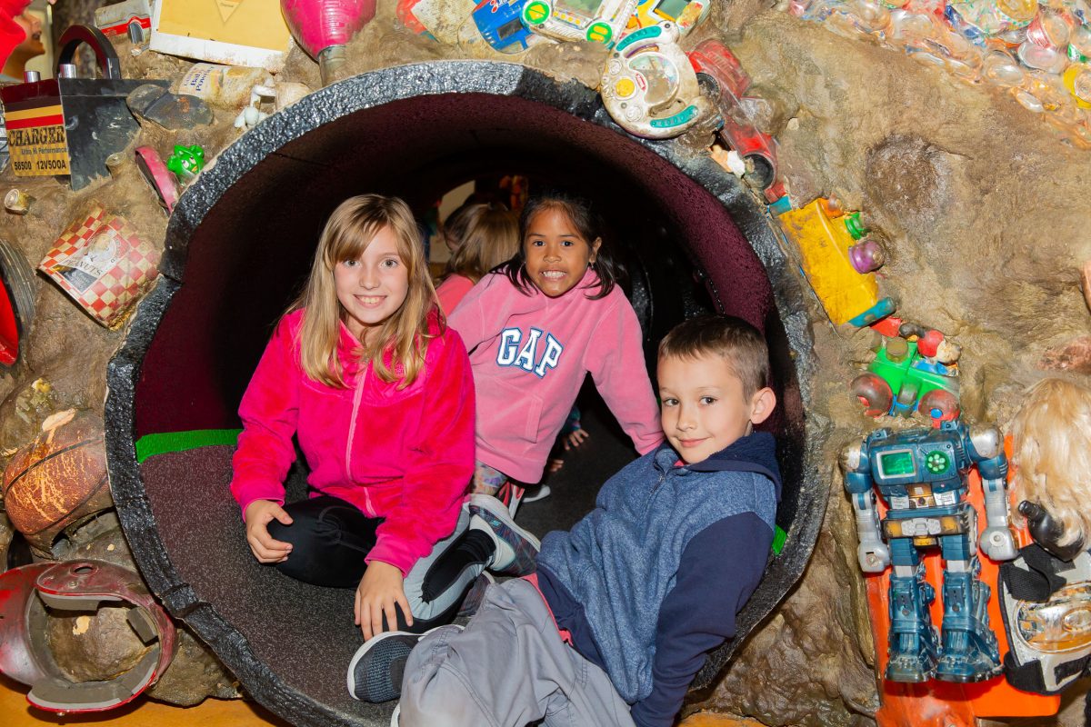 Children sitting in a tunnel through a fake trash pile