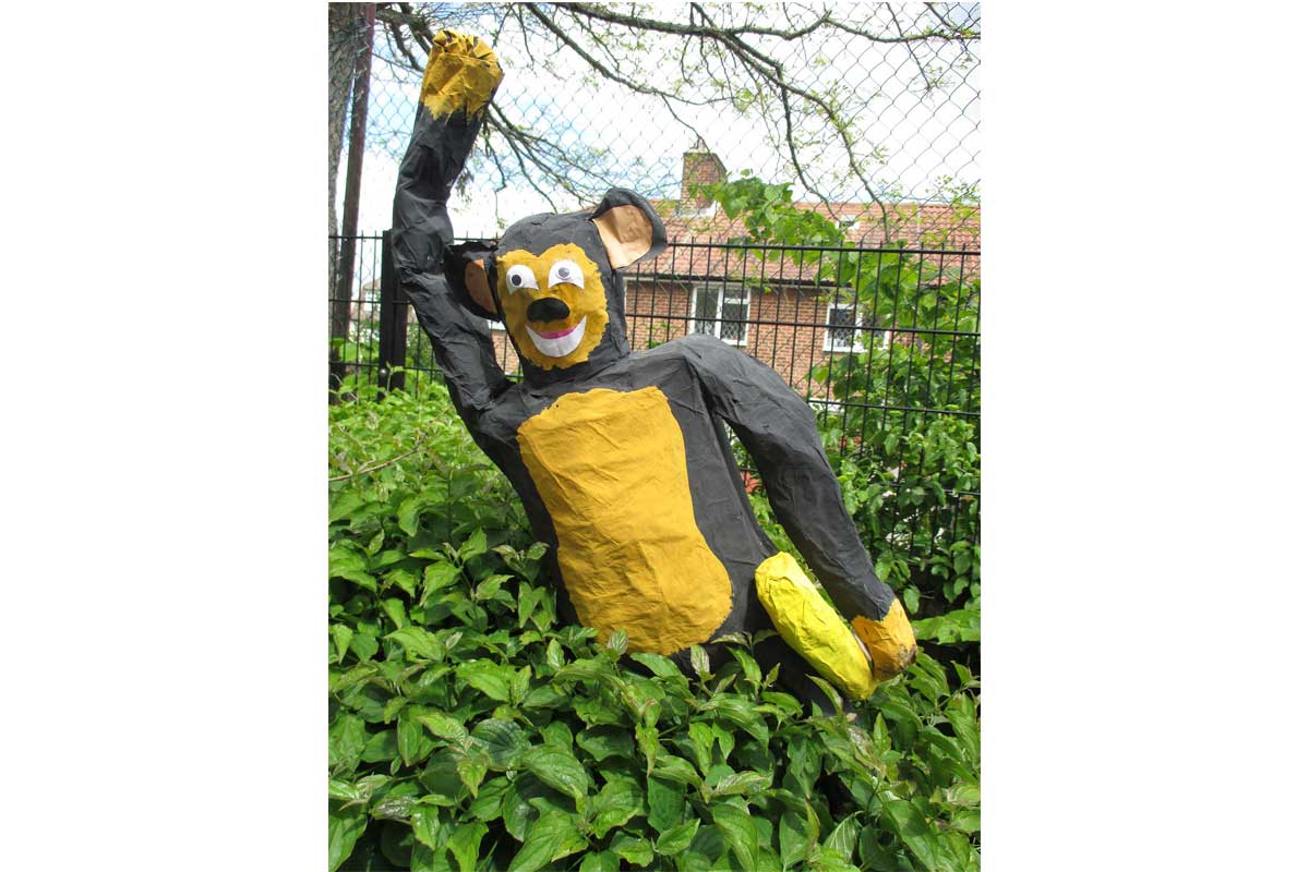 Papier mache monkey appearing out of a bush