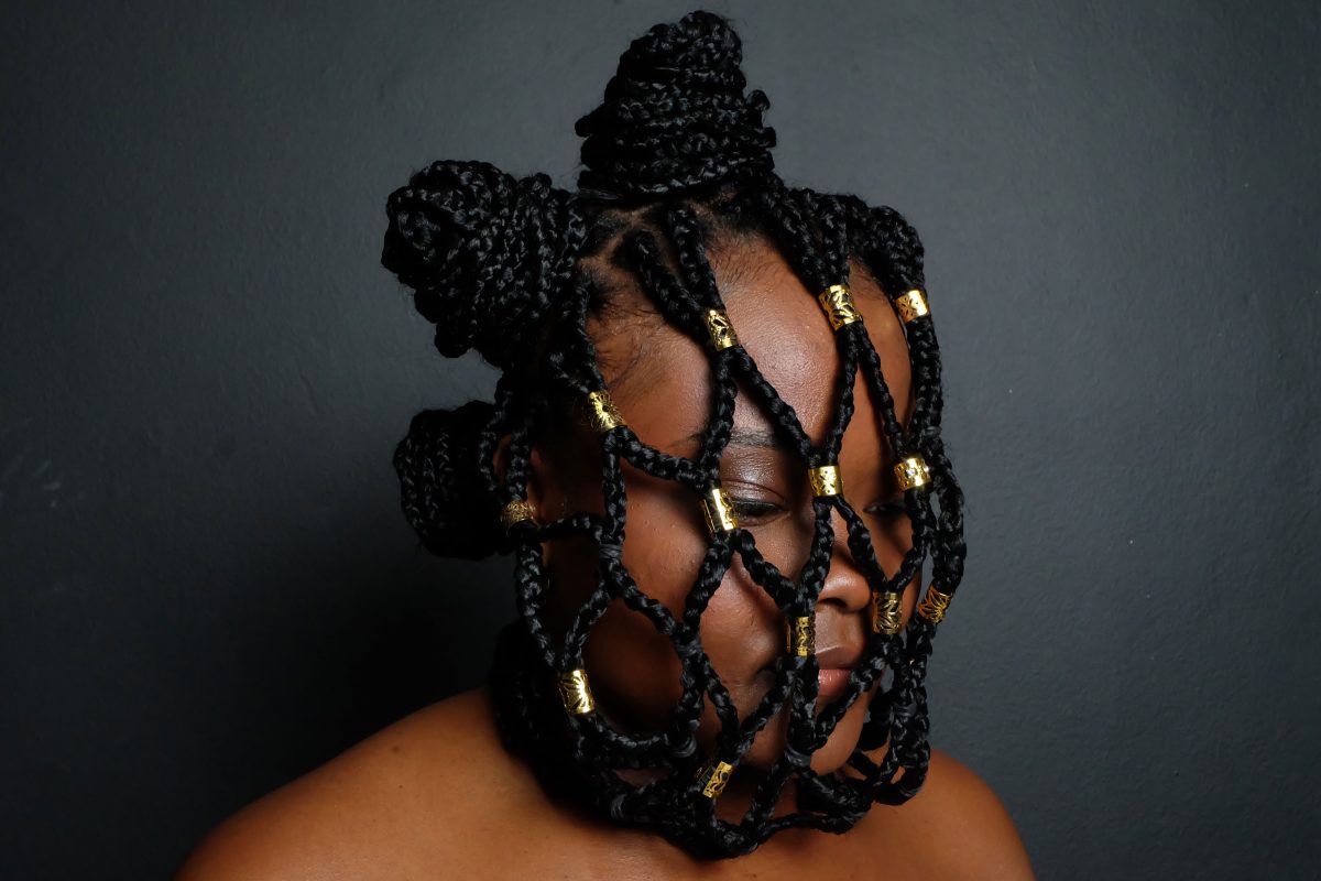 A portrait of a Black woman with her hair styled into chainmail type pattern falling over her face