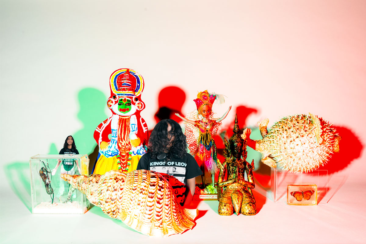 Woman stands with hair over her face, with shells and figurines around her