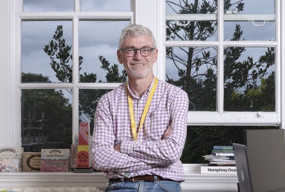 Gordon Seabright smiles into the camera as he leans on a table in his office