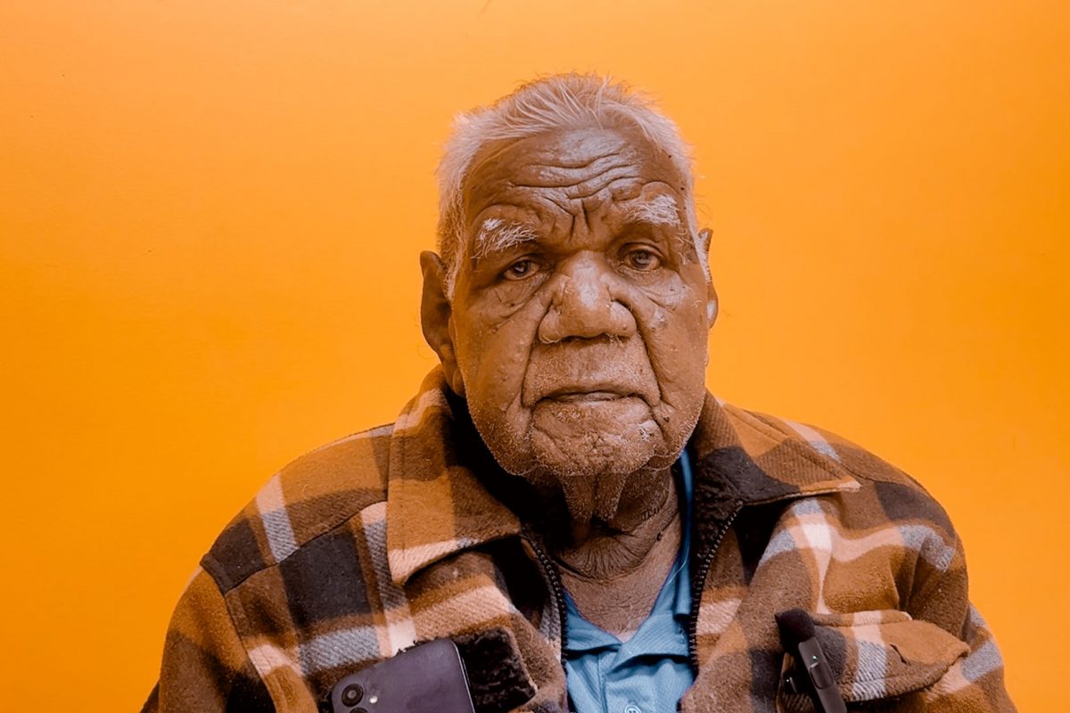 Mr Michael Jones portrait, a Warumungu senior man, sat in front of an orange background