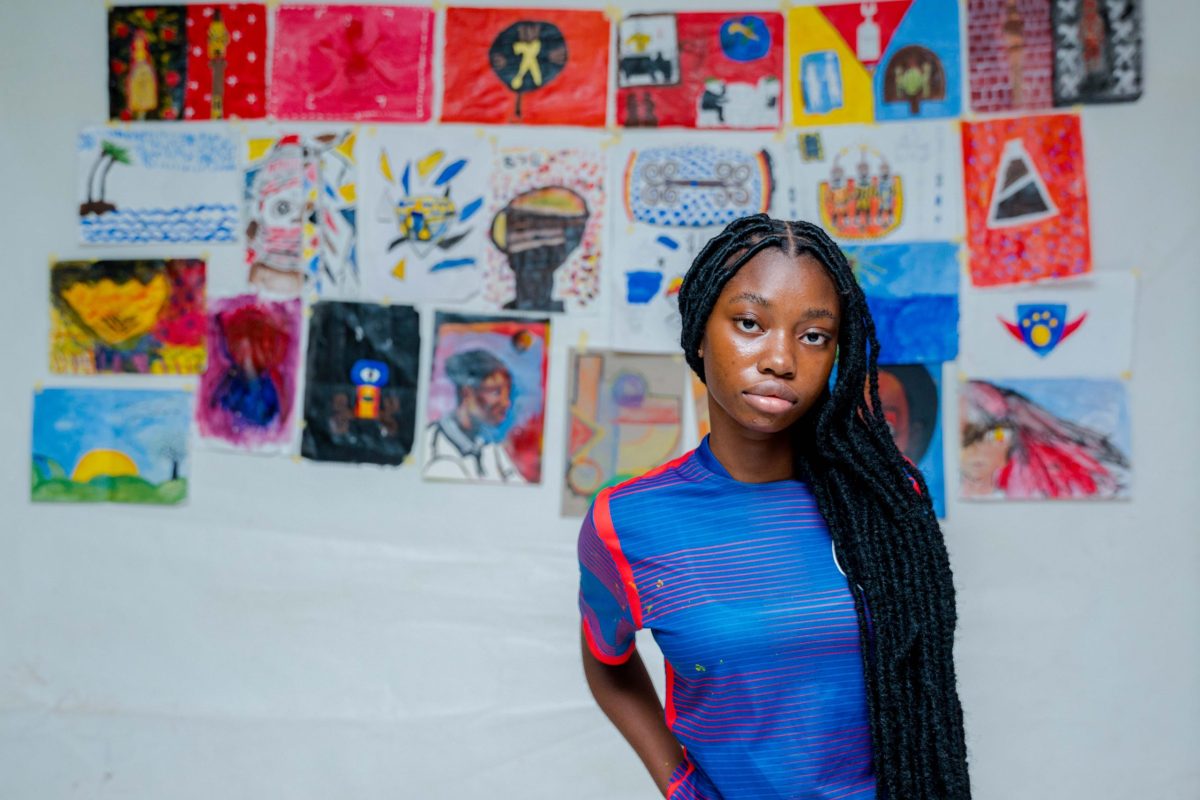 A young woman standing in front of a wall displaying young people's artworks