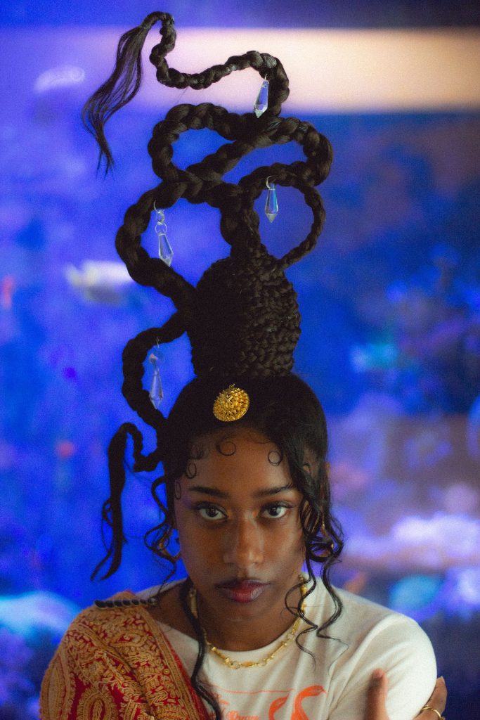 Faith Bloomer, a black women with an elaborate hair style, sits in front of an aquarium