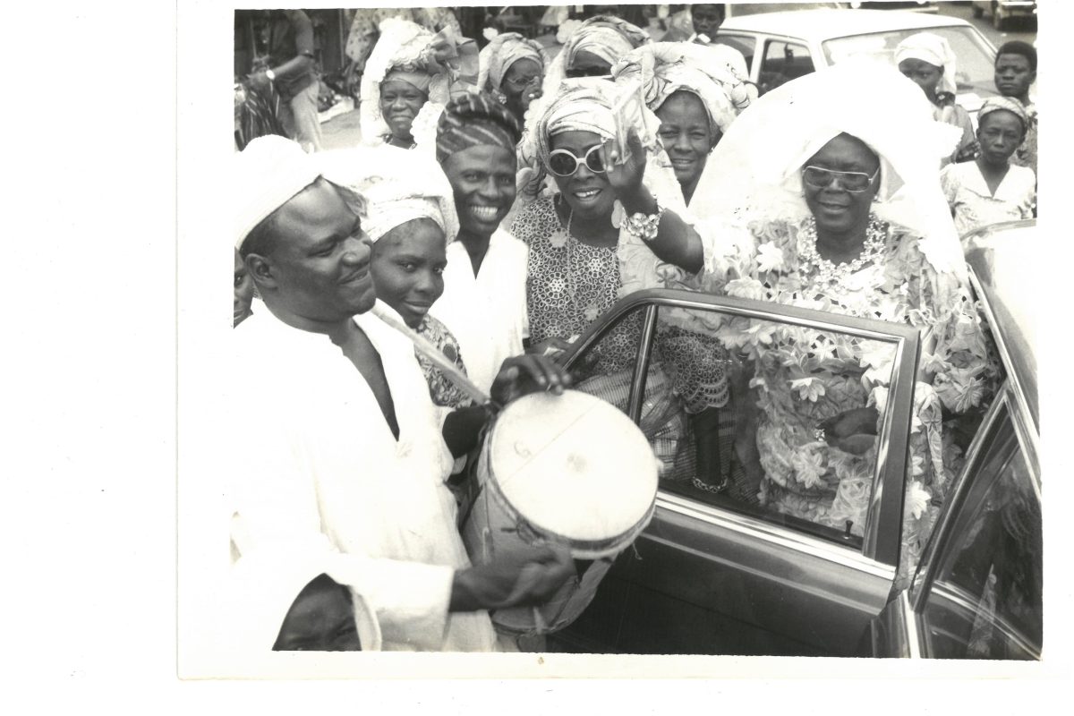 Black and white archive photo of a crowd of pepole, some of whom are playing talking drums