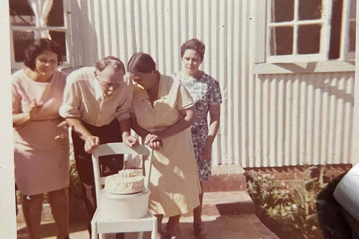 Archive photo of a cake on a chair, being blown out by a man who is surrounded by three women