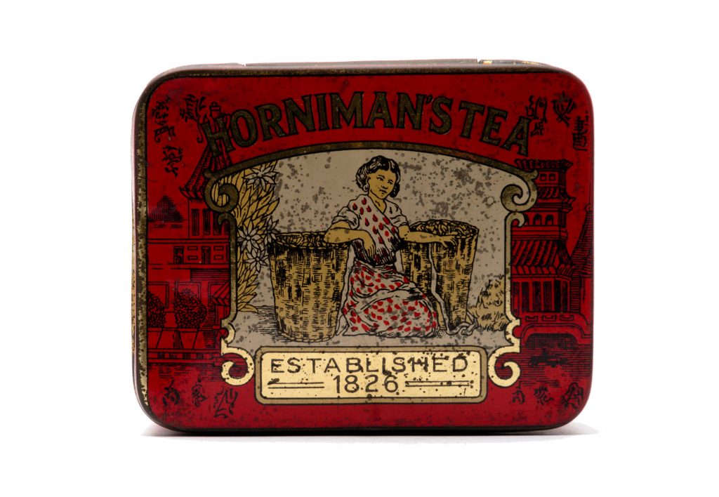 Red Horniman's Tea caddy featuring a woman sat next to two baskets of tea